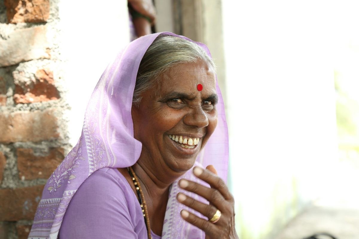 An older woman in a lilac sari laughing.