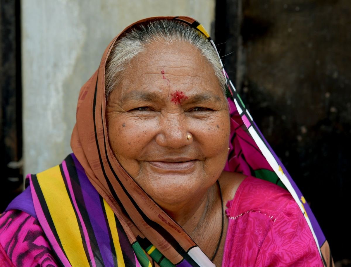 An older woman in a bright headscarf smiling.
