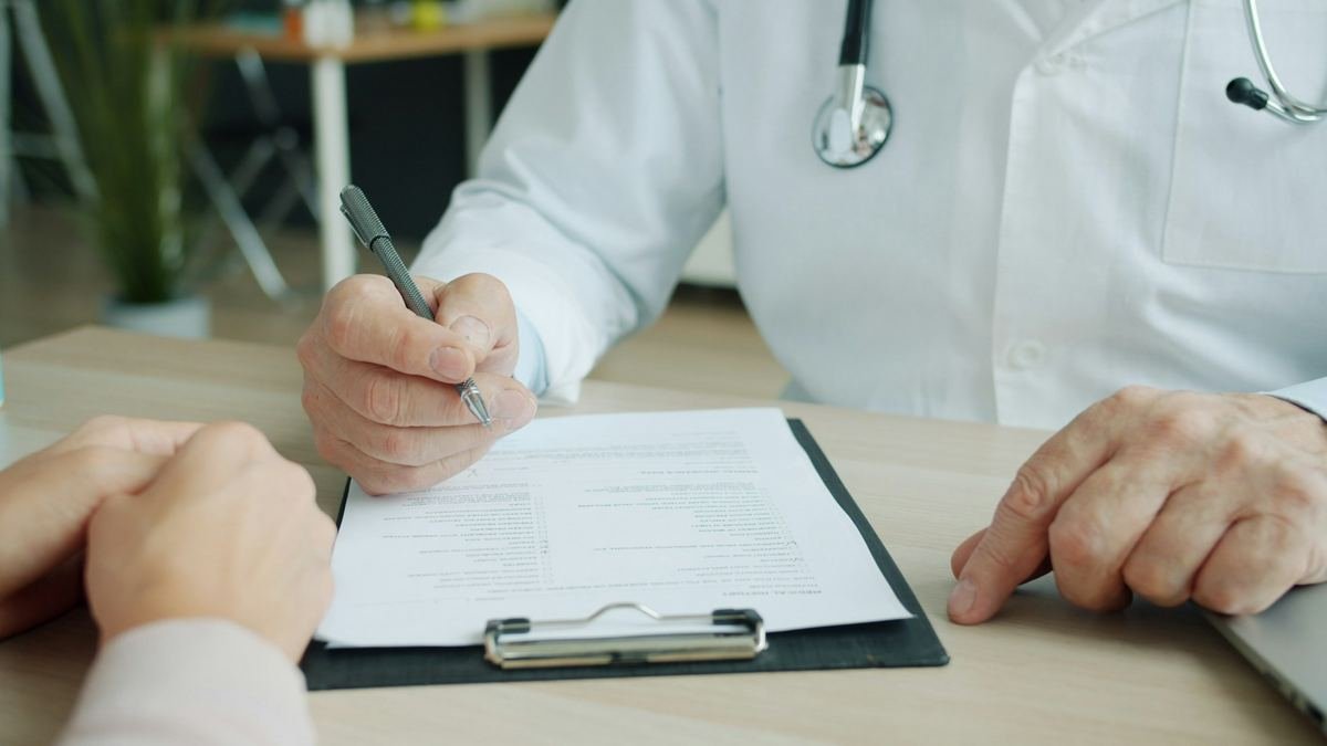 A doctor writing notes on a clipboard during a consultation.
