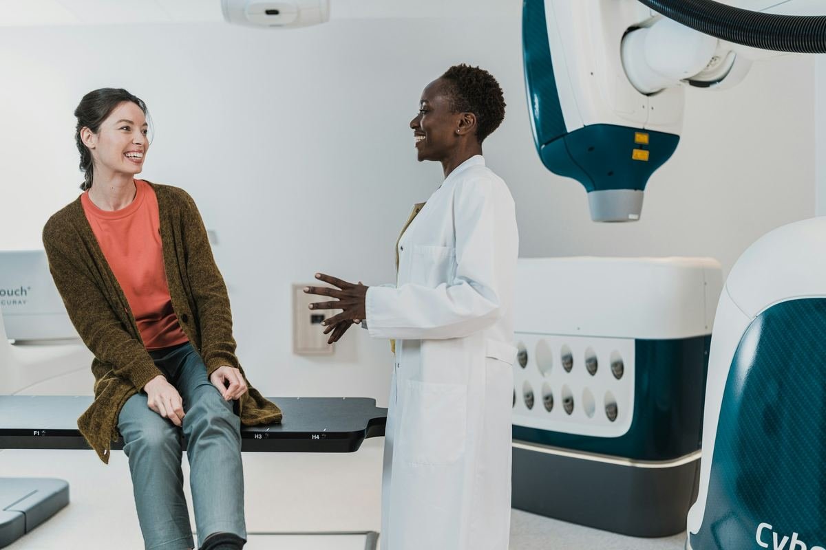 A doctor talking with a patient beside imaging equipment in a clinic.