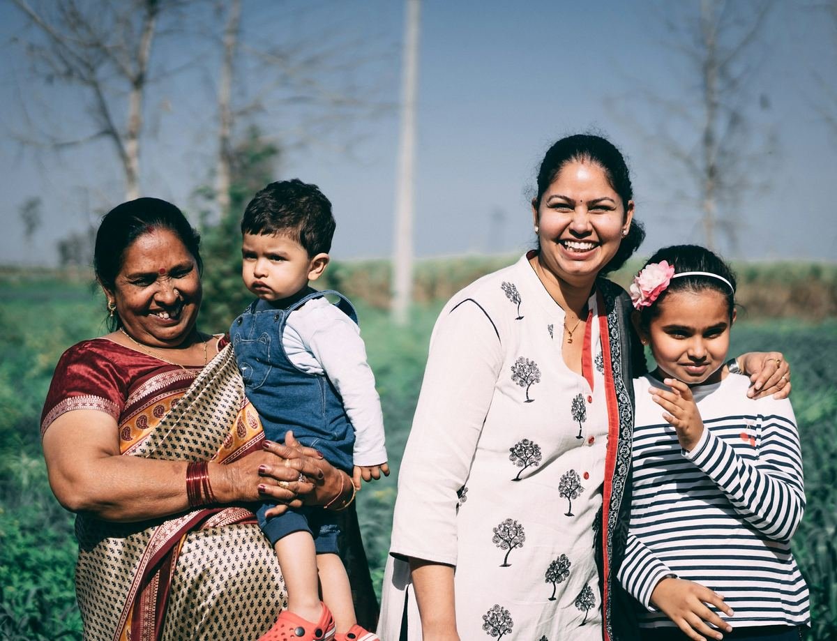 A smiling family with a grandmother and young child outdoors.