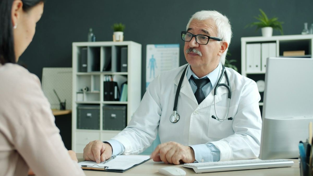 A senior doctor explaining something to a patient across a desk.