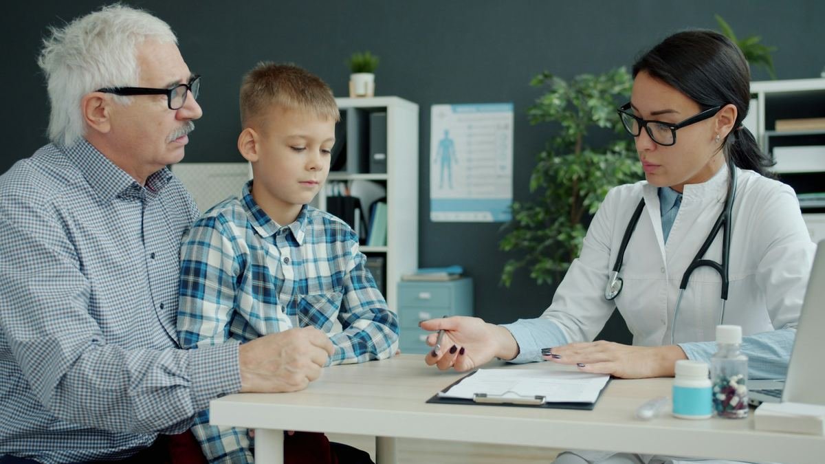 A doctor talking with a grandfather and grandson at a desk.