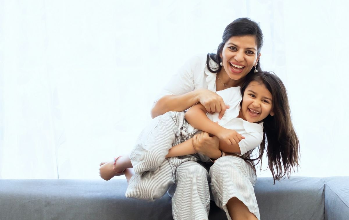 A mother holding her laughing daughter on a sofa.