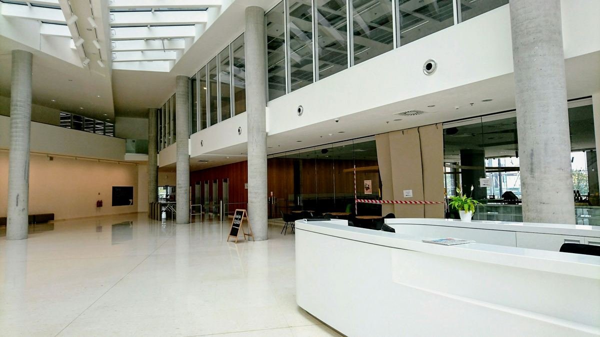 A bright double-height reception hall with a white desk.