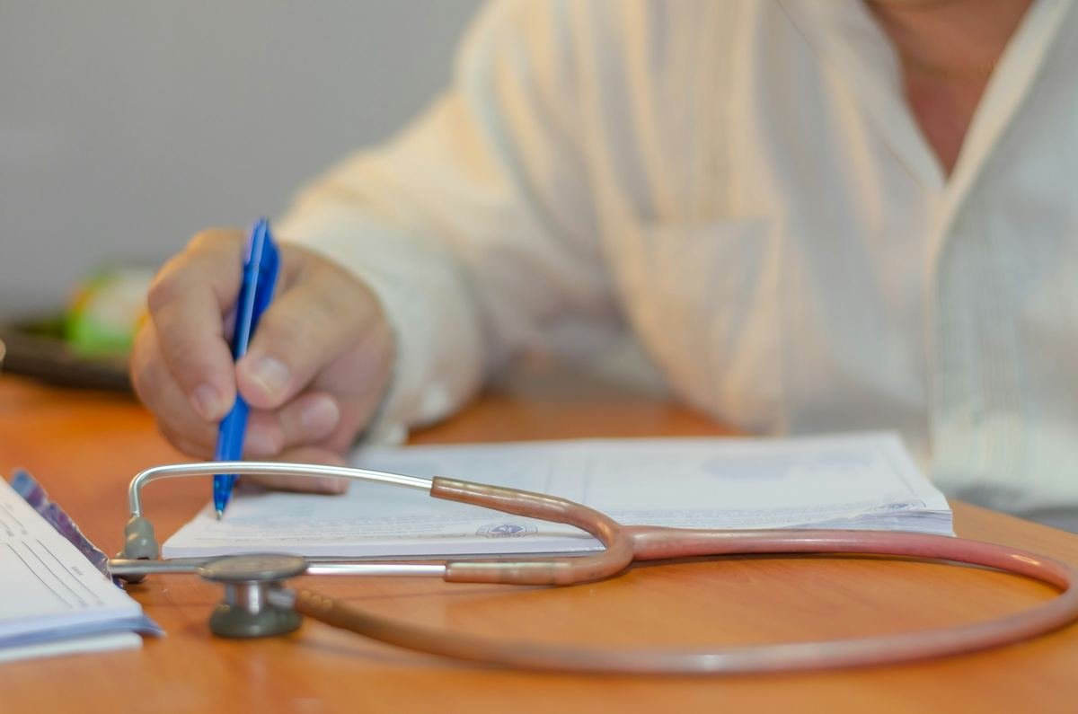 A clinician writing notes beside a stethoscope.