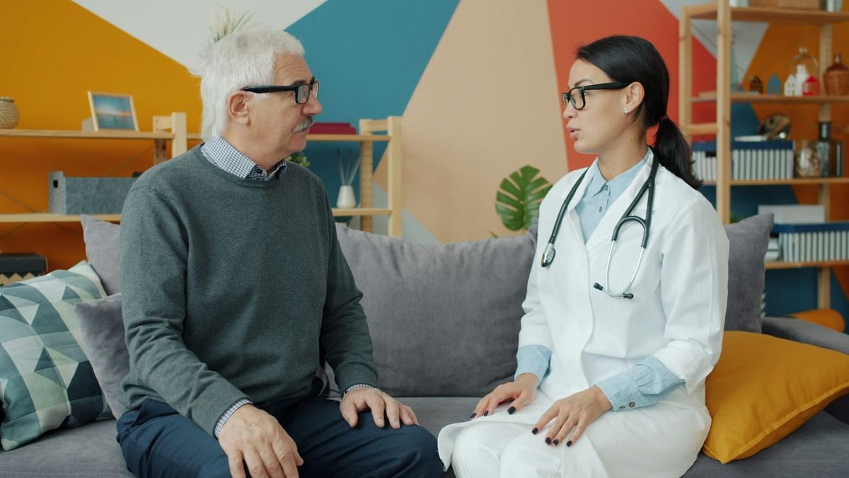 A doctor talking with an older man on a sofa.