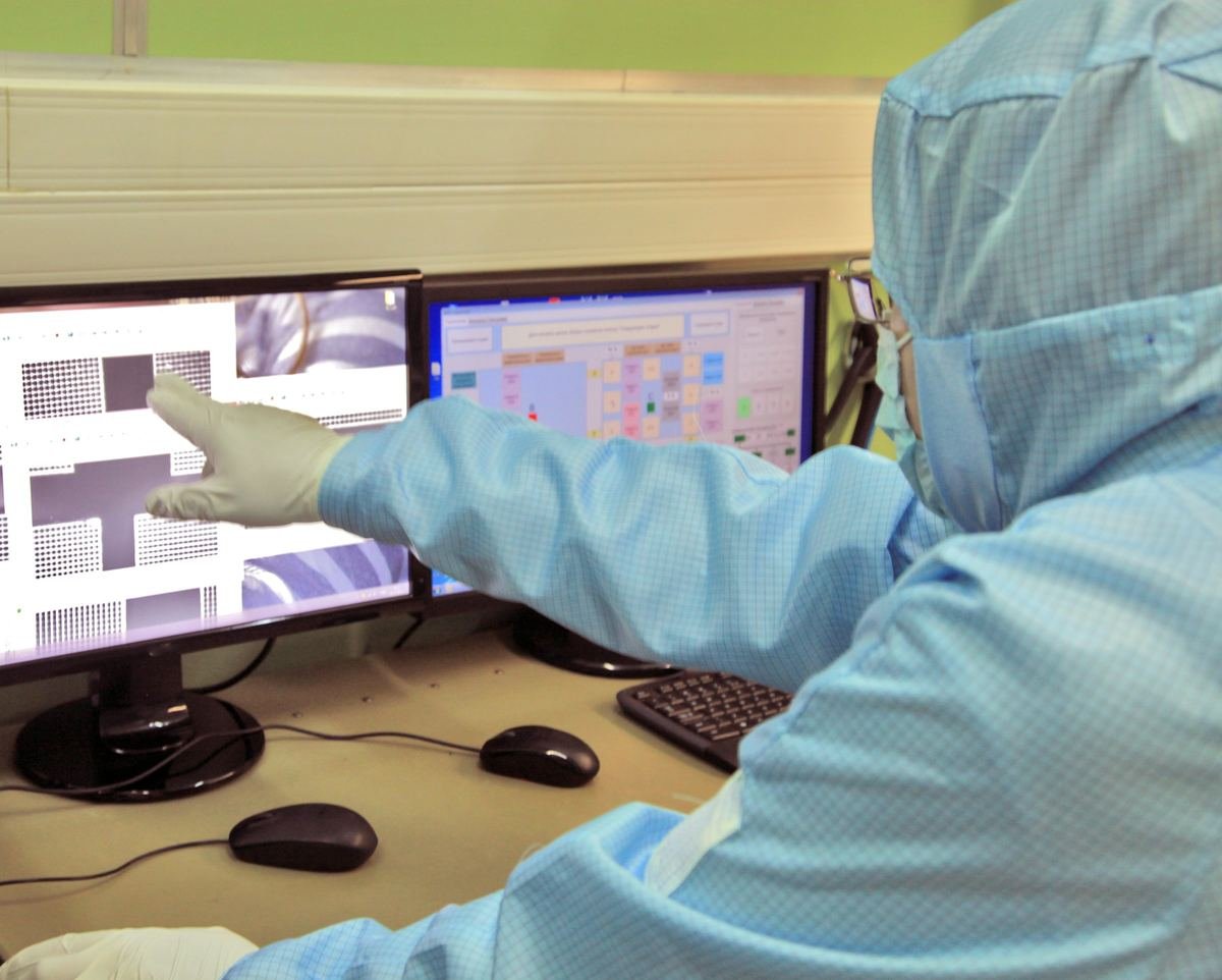 A scientist in protective clothing pointing at results on a screen.
